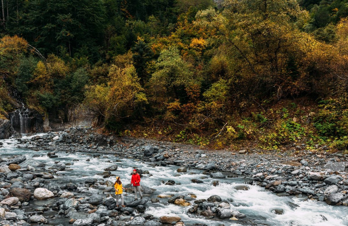 A couple of tourists walking along a mountain river in autumn. Active rest on the nature. An active couple is engaged in Hiking. A young couple is engaged in tracking. Copy space