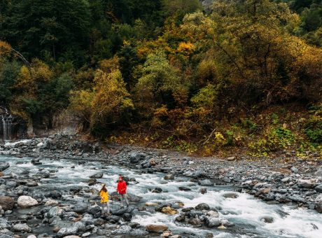 A couple of tourists walking along a mountain river in autumn. Active rest on the nature. An active couple is engaged in Hiking. A young couple is engaged in tracking. Copy space
