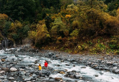 A couple of tourists walking along a mountain river in autumn. Active rest on the nature. An active couple is engaged in Hiking. A young couple is engaged in tracking. Copy space